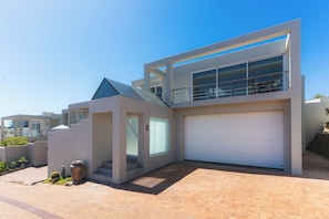Een modern herenhuis met garage, balkon en een klein buitenstuk met planten.