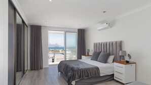 Een moderne slaapkamer met een groot bed, een nachtkastje met lampen, een garderobe en uitzicht op de stad.