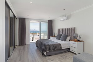 Een moderne slaapkamer met een groot bed, een nachtkastje met lampen, een garderobe en uitzicht op de stad.
