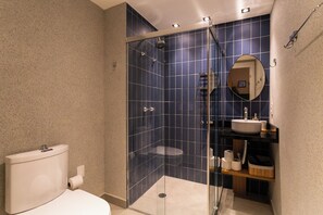 Un baño moderno con ducha de vidrio, inodoro blanco y lavamanos con espejo arriba.