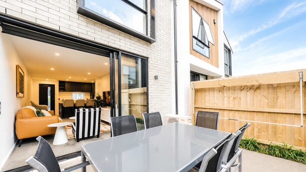 A modern outdoor patio with a glass table and chairs, a sofa, and a wooden fence. - Addington 2BR with Patio & Parking | Near Hagley (Christchurch)