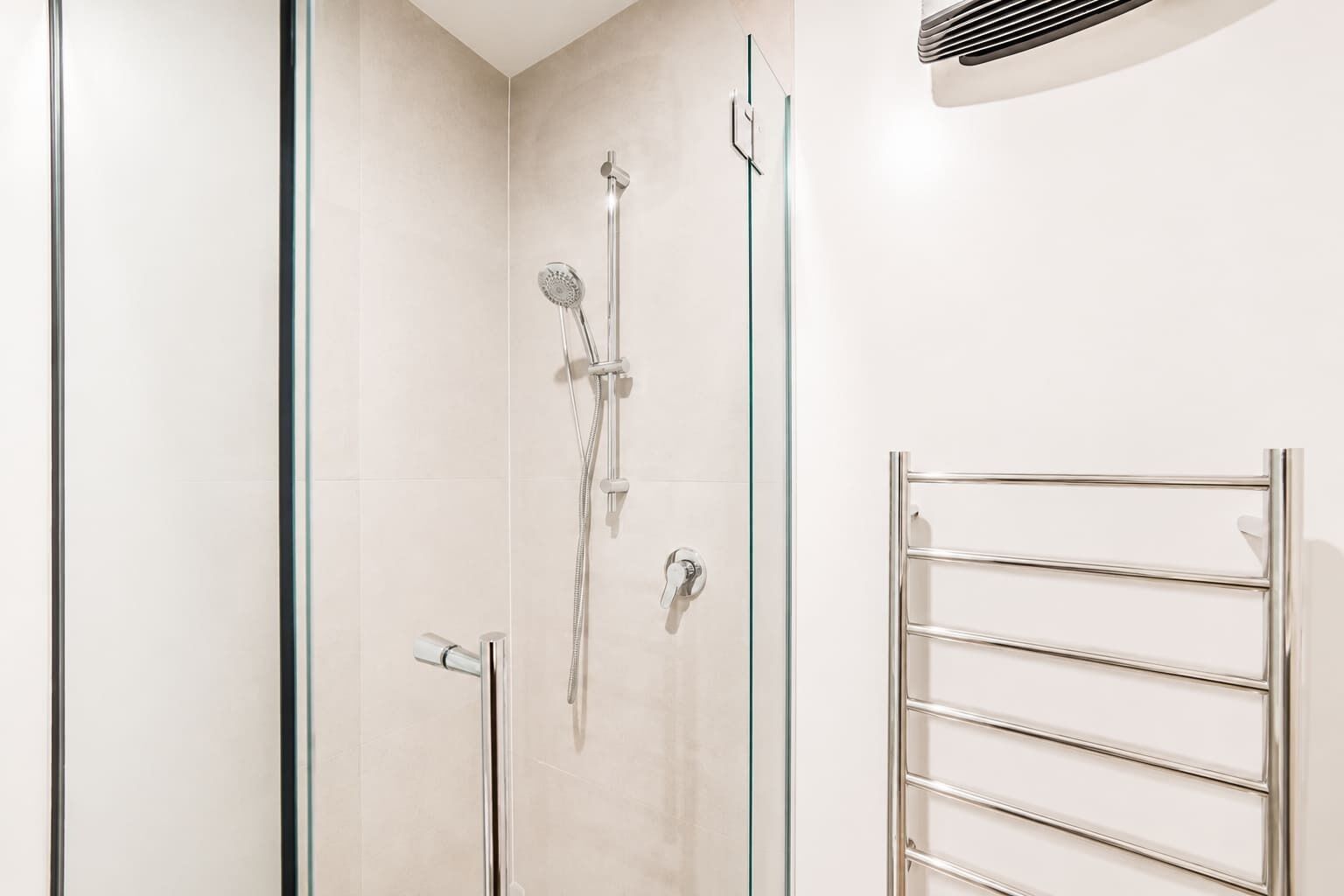 Un baño moderno con cabina de ducha de vidrio, un perchero de cromo y un respiradero empotrado en la pared.