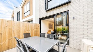 En moderne udendørs terrasse med et glasbord og stole, et træhegn og en murstensvæg.
