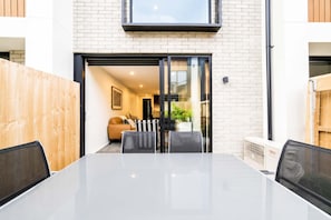 Un intérieur moderne avec une porte vitrée donnant sur un espace de vie, une table à manger avec des chaises et un appareil de climatisation visible.