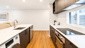 A modern kitchen with a dishwasher, oven, and a window with blinds. - Addington 2BR with Patio & Parking | Near Hagley (Christchurch)