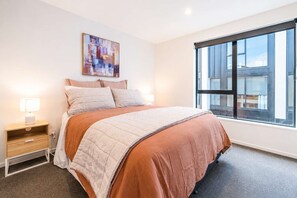 Une chambre à coucher avec un lit, une table de chevet, une lampe et une grande fenêtre.