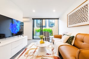 Un salon moderne avec un téléviseur à écran plat, un canapé blanc, une table basse agrémentée d’un vase et un tapis à motifs.