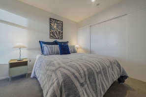 A bedroom with a bed, two bedside tables with lamps, a wall art piece, and a closet. - Stylish CBD Stay | 2BR | Private Deck (Christchurch)