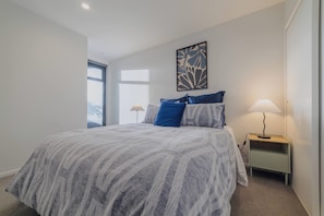 A bedroom with a large bed, a bedside table with a lamp, and a window. - Stylish CBD Stay | 2BR | Private Deck (Christchurch)