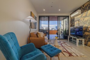 A modern living room with a sofa, blue armchairs, a coffee table, and a TV. - Stylish CBD Stay | 2BR | Private Deck (Christchurch)