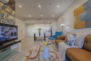 A modern living room with a flat-screen TV, a sofa, a coffee table, and a dining area in the background. - Stylish CBD Stay | 2BR | Private Deck (Christchurch)