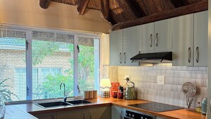 Eine moderne Küche mit Strohdach, fest eingebautem Herd und einem großen Fenster mit Jalousien.