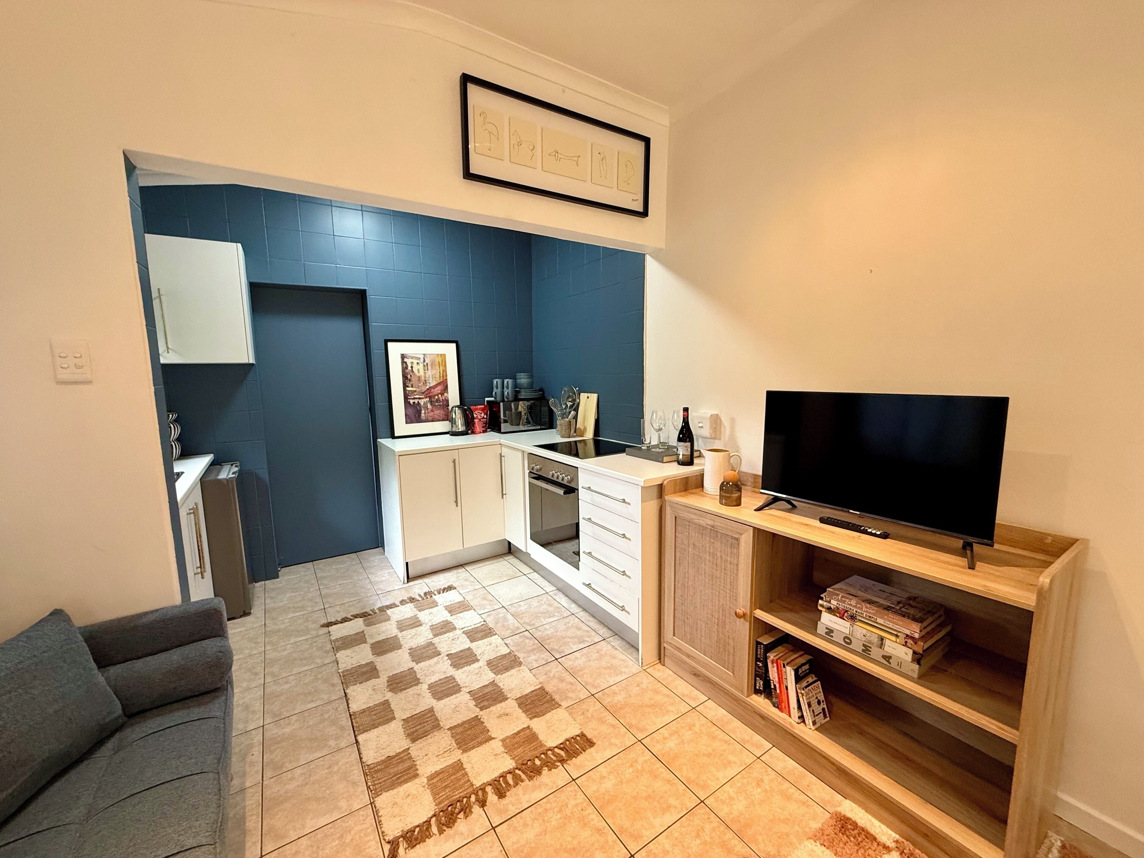 Un espacio habitable compacto con kitchenette, televisor de pantalla plana, sofá y estantería.