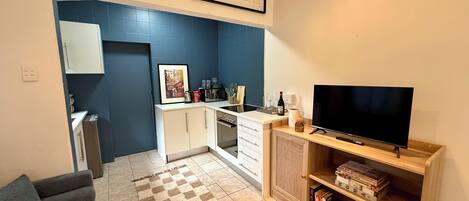 Un espacio habitable compacto con kitchenette, televisor de pantalla plana, sofá y estantería.