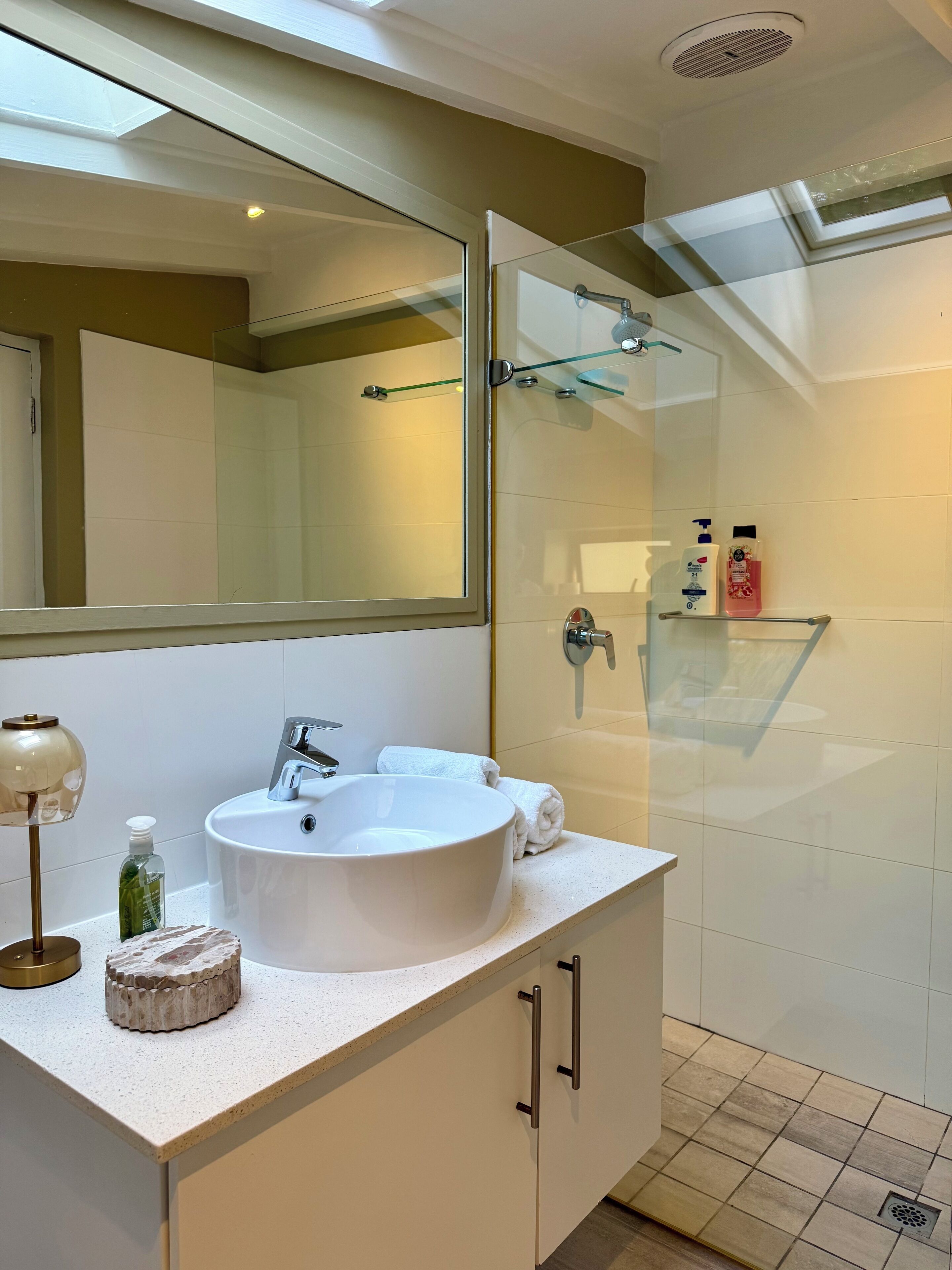 A modern bathroom with a large mirror, a white sink, and a glass shower enclosure.