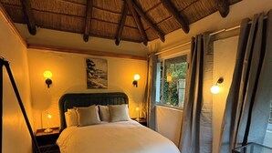 Ein Schlafzimmer mit Bett, Nachttisch, Stehlampe, einem Fenster mit Vorhängen und einer Decke mit Holzbalken.