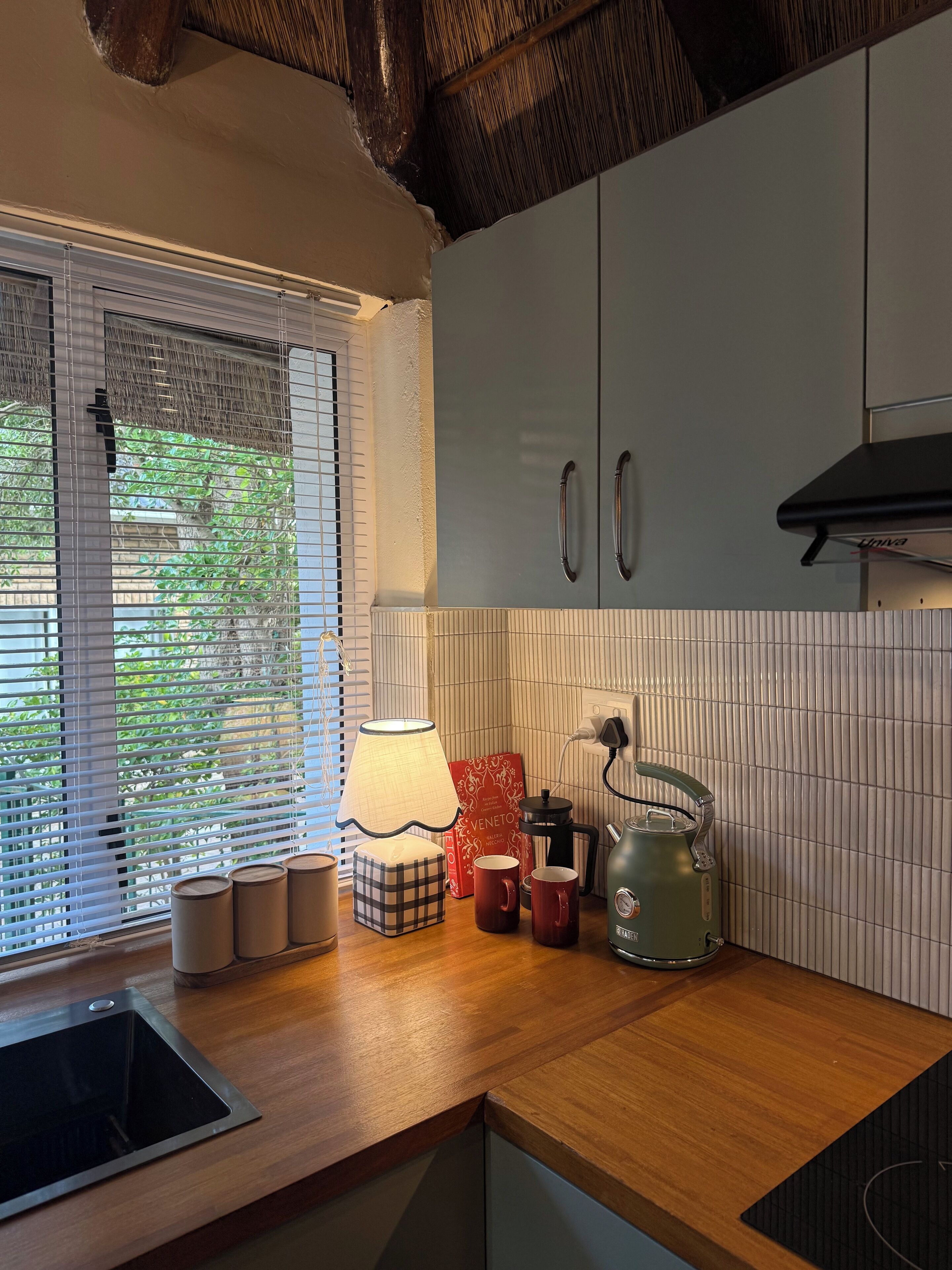 A modern kitchen with a wooden countertop, a built-in stove, and a window with blinds.