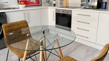 A modern kitchen with white cabinets, a glass-top table, and two brown chairs.