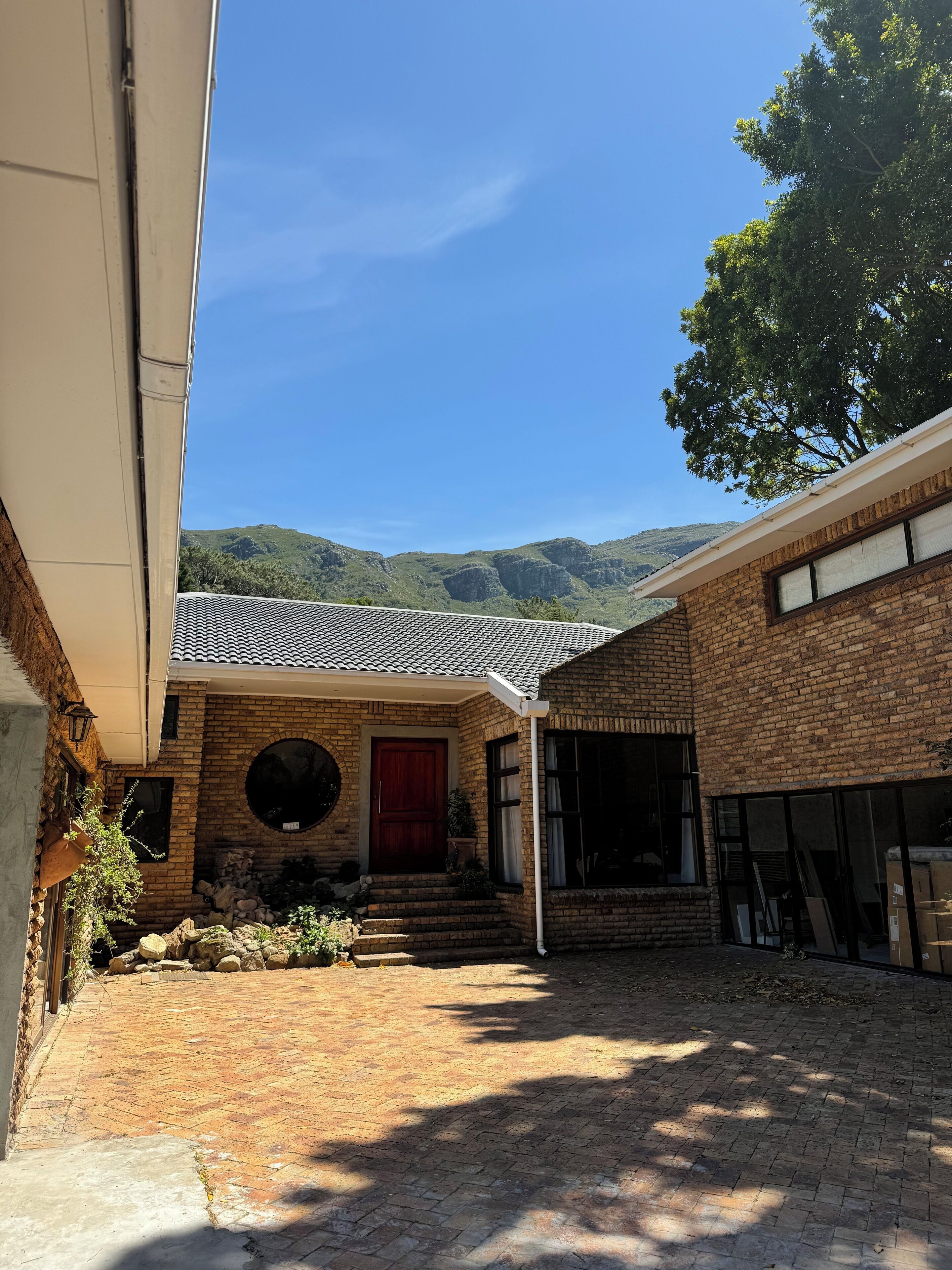 A courtyard with a brick building, a red door, and a view of green hills.
