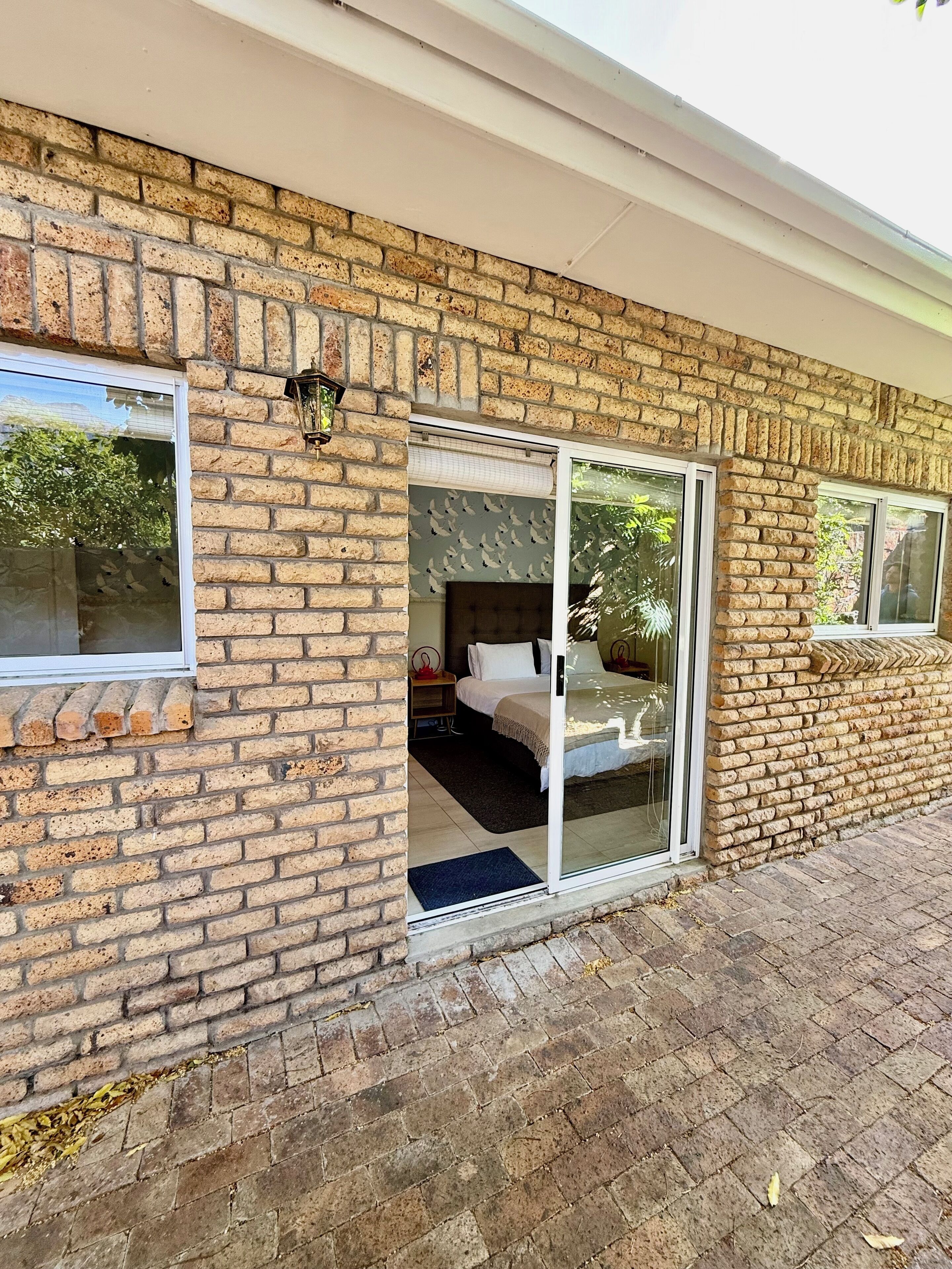 A brick exterior with a sliding glass door leading to a bedroom with a bed and a nightstand.