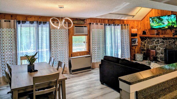 A cozy living room with a fireplace, a TV mounted on the wall, and a dining area with a table and chairs. - Modern Mountain Escape – Fun Filled Retreat! (Bartlett)