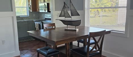 A dining area with a wooden table and chairs, a sailboat decoration, and a view of the kitchen through an open doorway.