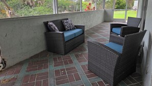 Ein überdachter Patio-Bereich mit Korbmöbeln und Blick auf Grünflächen.