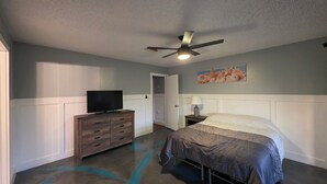 Ein Schlafzimmer mit einem Bett, einem Schminktisch, einem Fernseher, einem Deckenventilator und einem Bild an der Wand.