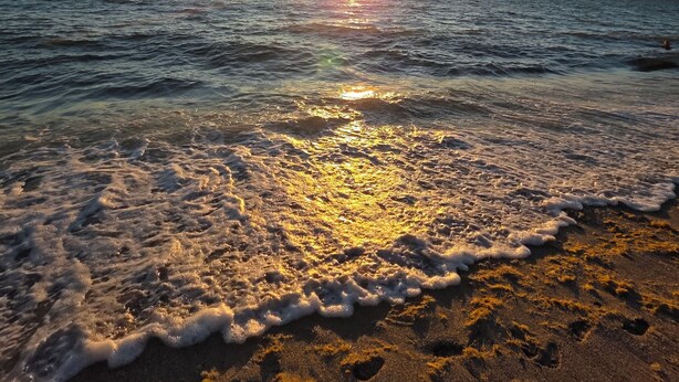 Ein Strand, an dem sanft Wellen an die Küste branden, während die Sonne in der Ferne untergeht.