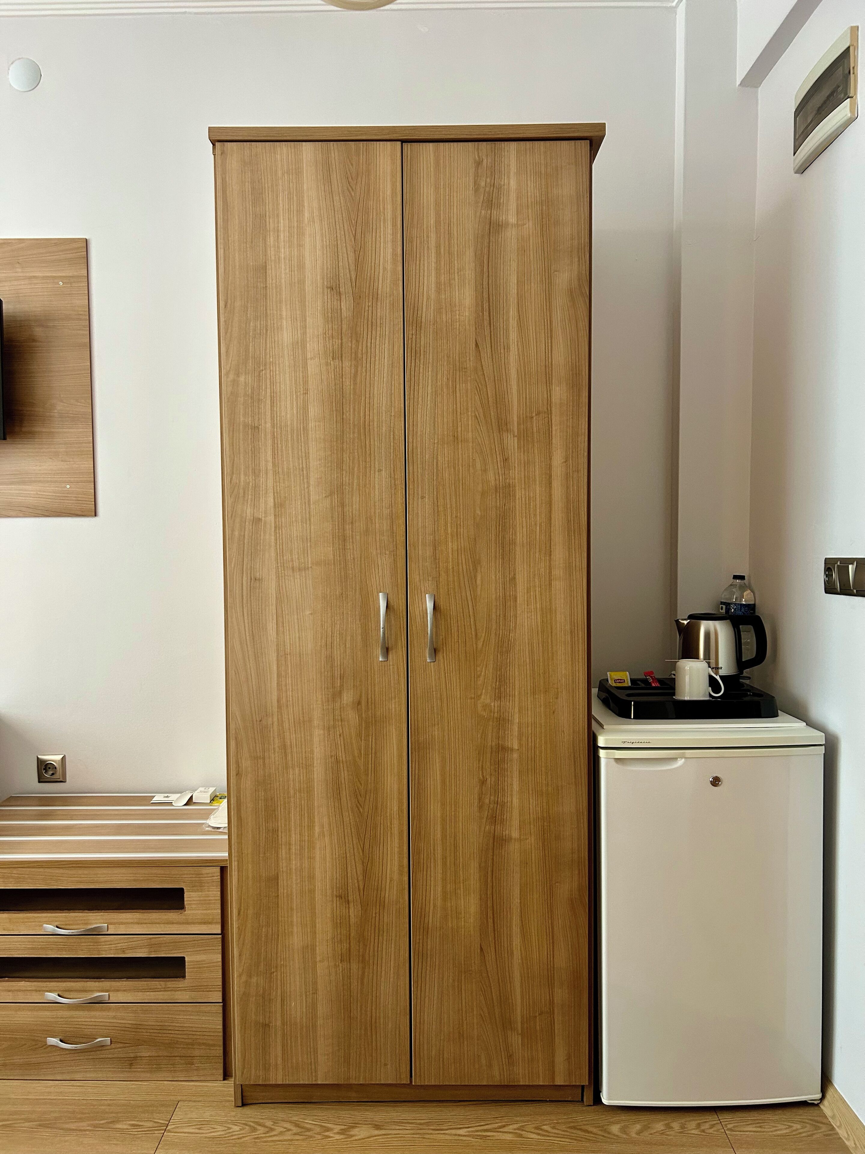 Une armoire en bois à deux portes, avec un petit réfrigérateur blanc placé à côté.