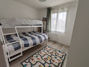 Une chambre avec un lit superposé, une fenêtre, un radiateur et un tapis à motifs.