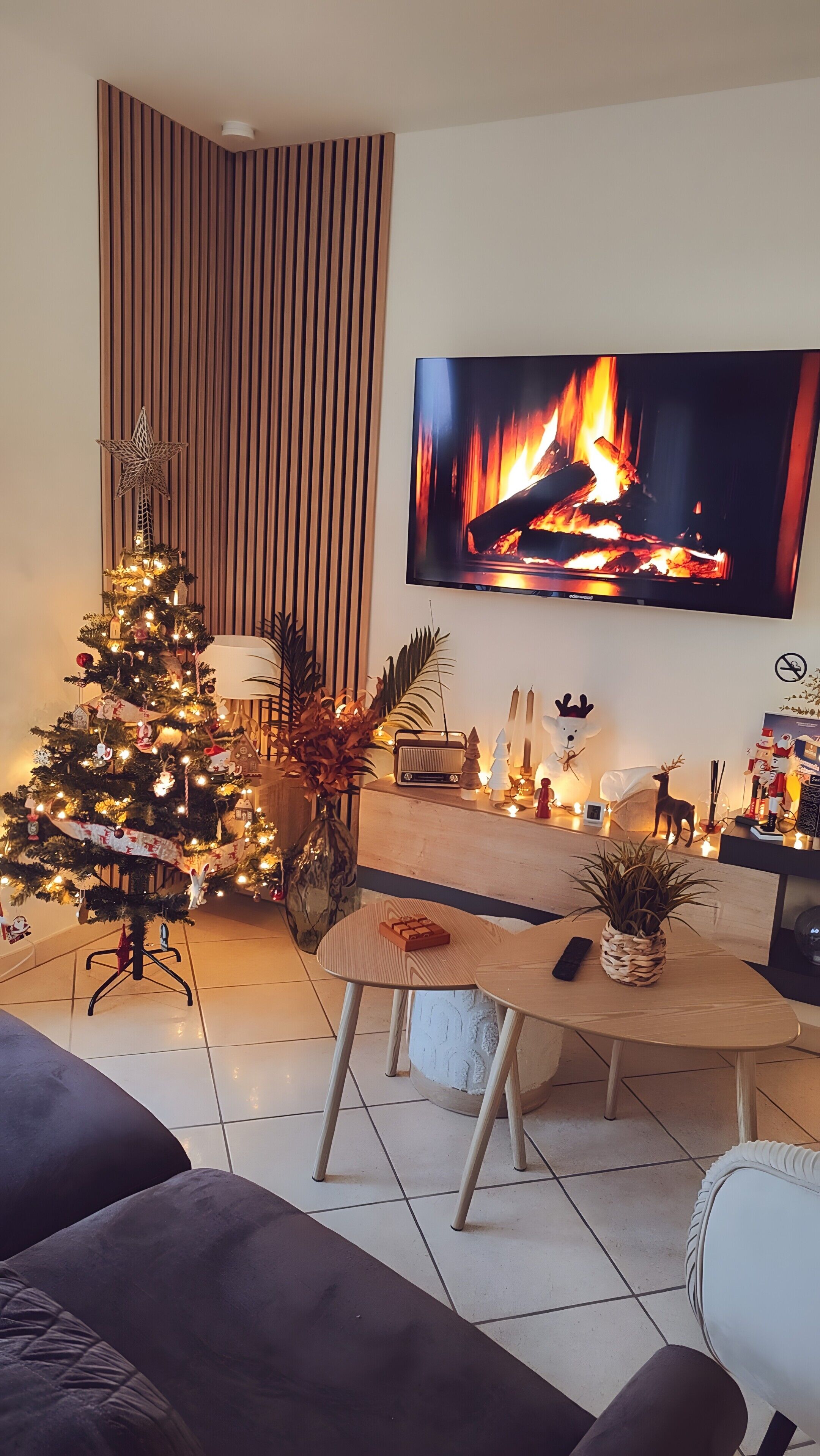 Un salon avec un téléviseur diffusant une image de cheminée, d’un sapin de Noël et d’un coin salon confortable.