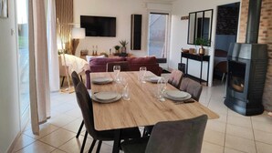 A dining area with a wooden table set for six, a sofa, a TV, and a fireplace.