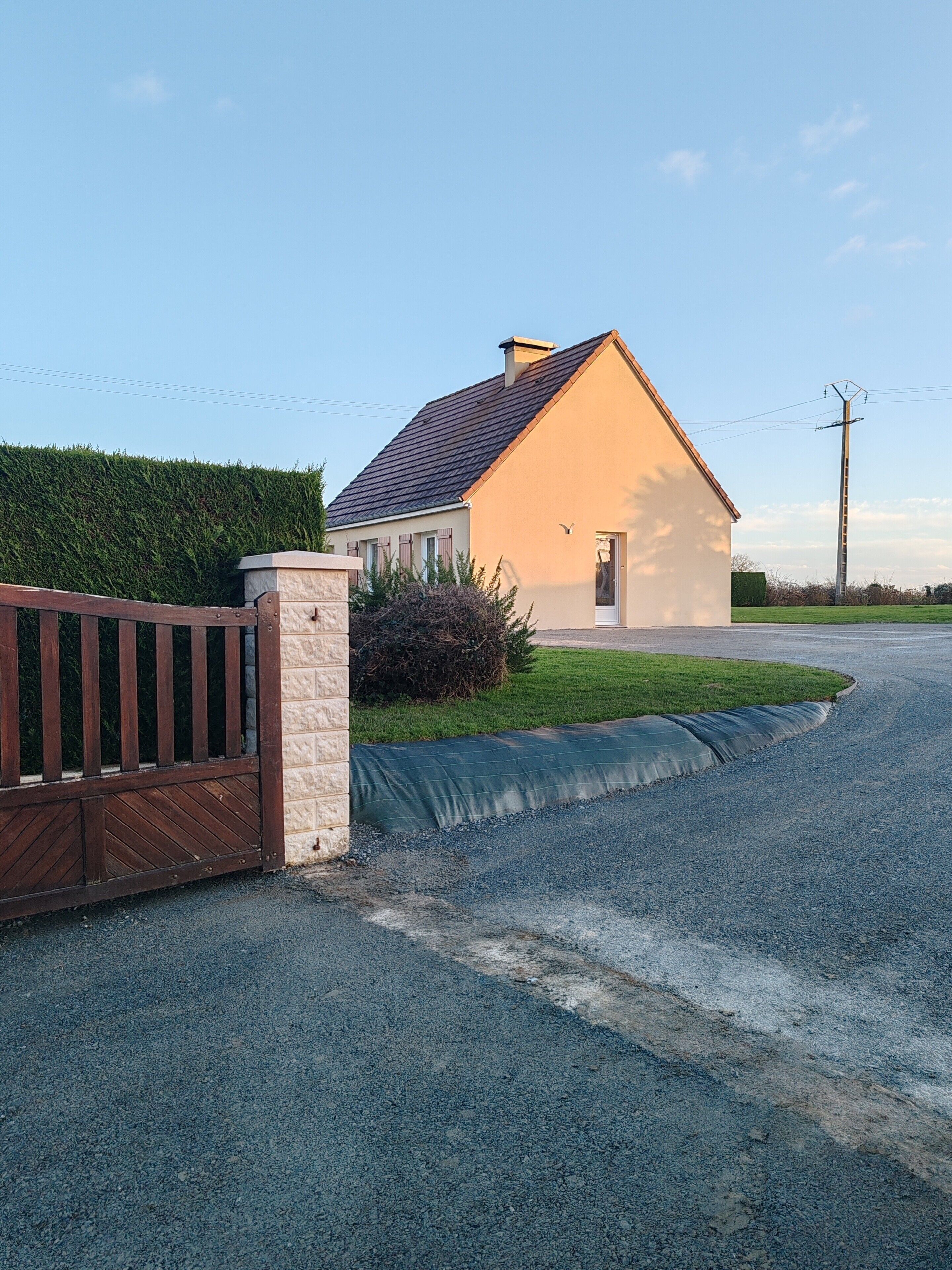 A house with a gated driveway, a stone pillar, and a grassy lawn.