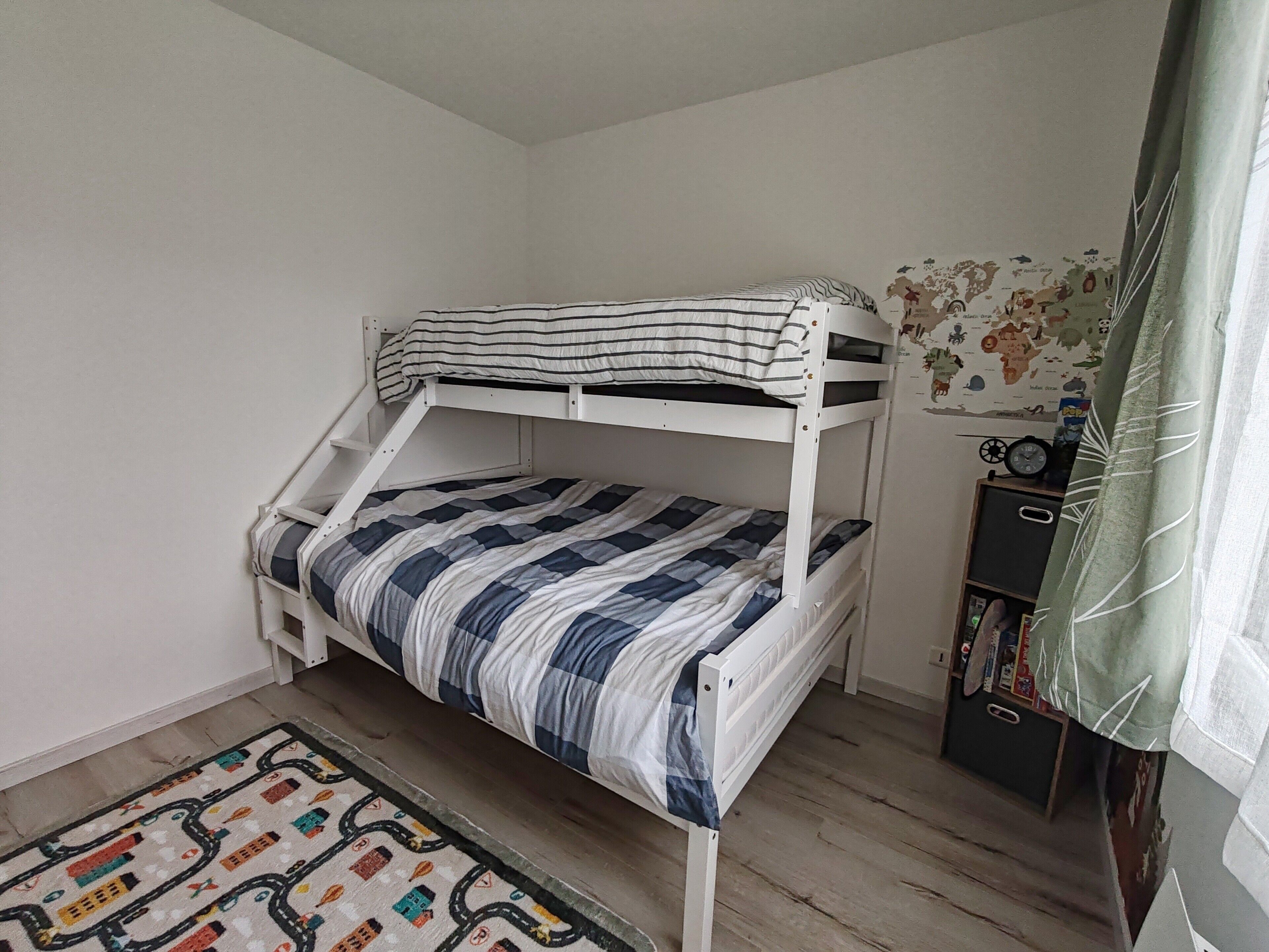 Een stapelbed met gestreepte beddengoed, een wereldkaart aan de muur, een boekenkast en een tapijt met een patroon.