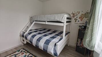 Een stapelbed met gestreepte beddengoed, een wereldkaart aan de muur, een boekenkast en een tapijt met een patroon.