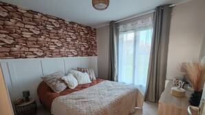 A bedroom with a stone wall, a bed with multiple pillows, a bedside table, and a view of the outdoors through a window.