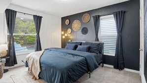 Een slaapkamer met een bed, donkere gordijnen, een raam en wanddecoratie.