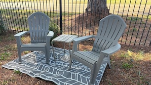 Dos sillas Adirondack sobre un piso de madera con un tapete estampado para exteriores.