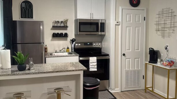Una cocina moderna con armarios blancos, electrodomésticos de acero inoxidable y una zona con taburetes de bar.