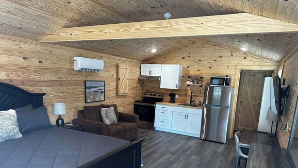 A compact room with a bed, a sofa, a small kitchen with a refrigerator, and a TV. - Cozy cabin in Starkville (Starkville)