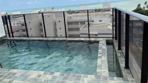 A rooftop pool with clear blue water, surrounded by a tiled deck and a glass balustrade. - Cozy and modern apartment with balcony. (João Pessoa)