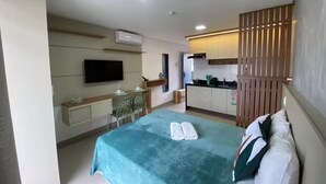 A hotel room with a bed, a desk, a TV, and a kitchenette. - Cozy and modern apartment with balcony. (João Pessoa)