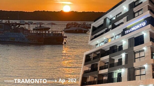 A modern building with a sign reading "TRAMONTO" and balconies overlooking a body of water. - Cozy and modern apartment with balcony. (João Pessoa)