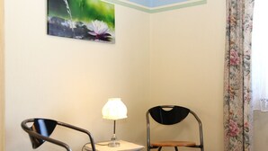 A corner room with a table, two chairs, a lamp, and a floral curtain. - Apartment 'Mit Garten' with Private Terrace, Private Garden and Wi-Fi (Medebach)