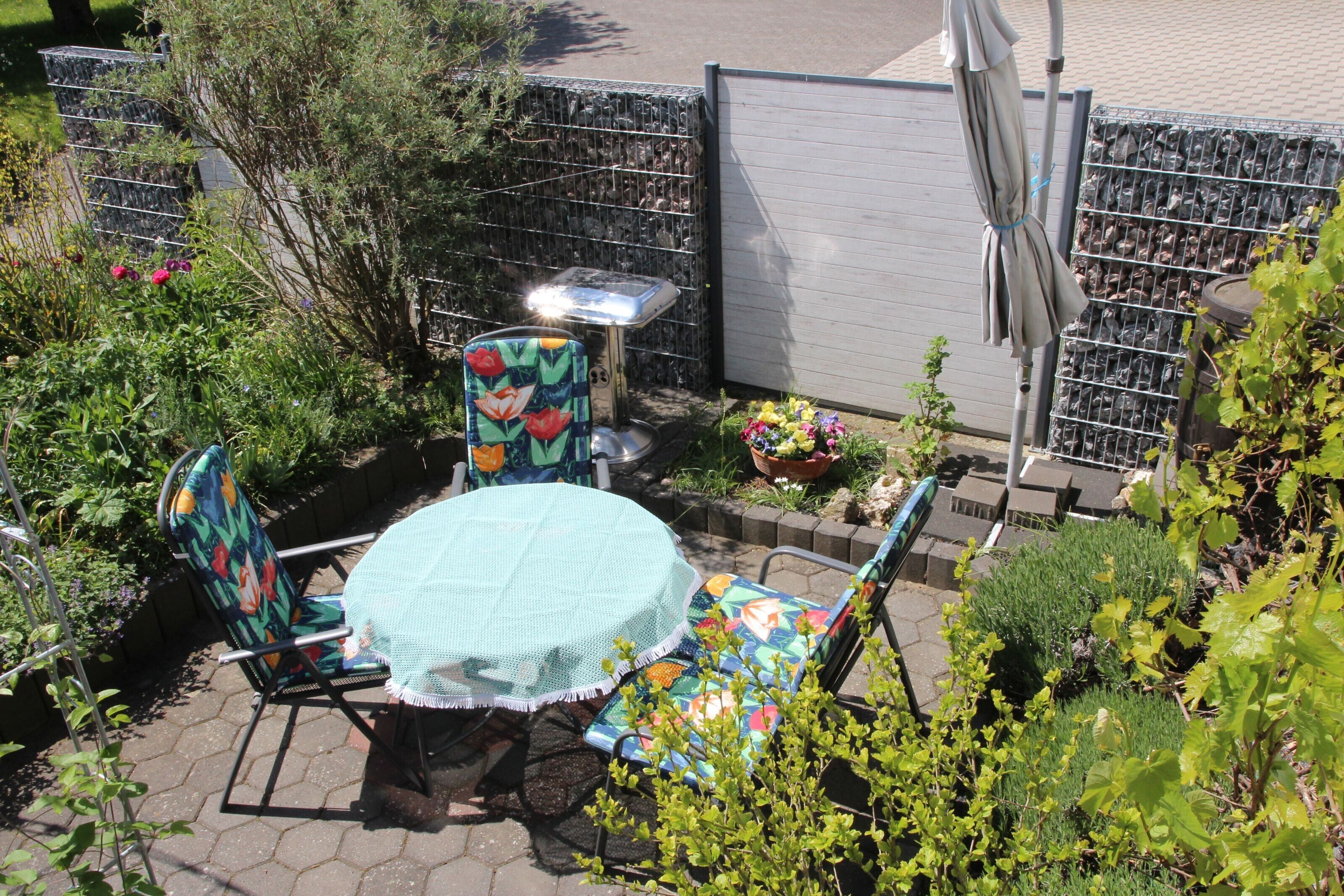 Een terras met een ronde tafel, twee stoelen en een bijzettafeltje met een lamp.