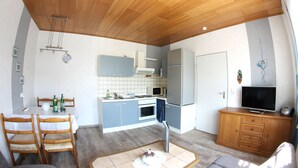 A compact kitchen with a microwave, oven, and refrigerator, a dining table with chairs, and a television on a wooden cabinet. - Apartment 'Mit Garten' with Private Terrace, Private Garden and Wi-Fi (Medebach)
