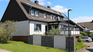 A two-story residential house with a sloped roof, a front porch, and a garage. - Apartment 'Mit Garten' with Private Terrace, Private Garden and Wi-Fi (Medebach)