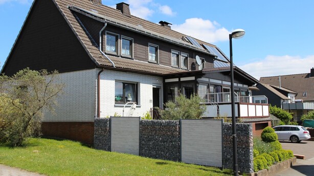 Ett tvåvåningshus med ett sluttande tak, en veranda och ett garage.