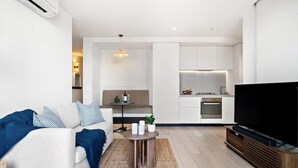 A modern living room with a sofa, a coffee table, and a flat-screen TV. - Cozy 1BR Melbourne Escape | Balcony | Pool | GYM (Melbourne)